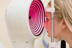 Young woman having her eyes examined by an eye handsome elderly doctor.